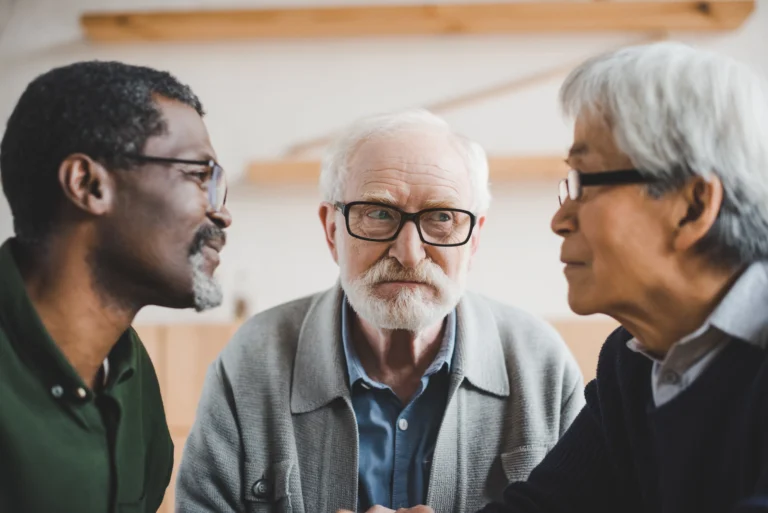 A group of elderly friends of different nationalities engaged in focused conversation at a table, symbolizing the importance of social activity in dementia care