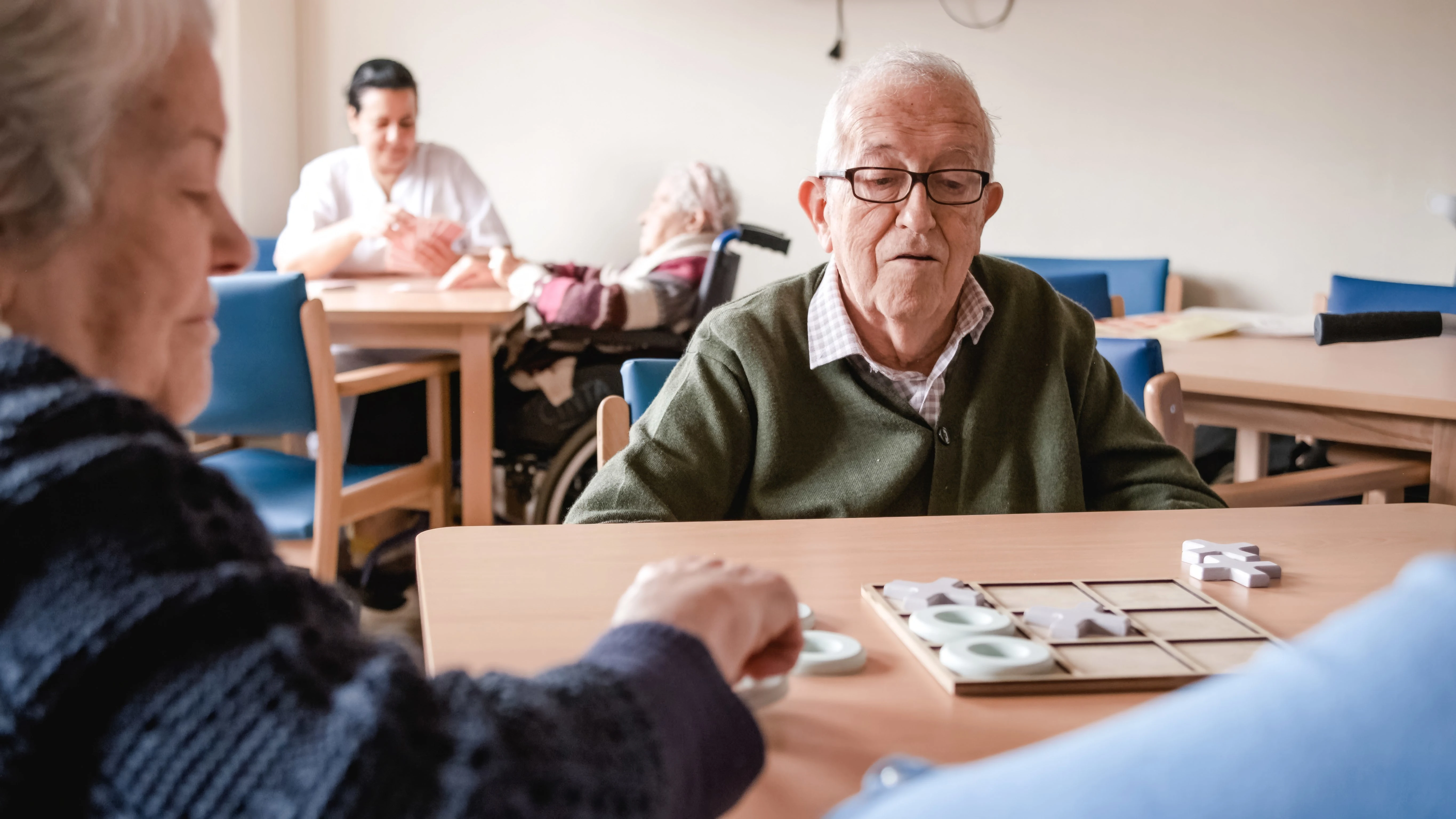 An elderly man playing tic-tac-toe with friends in a nursing home, encouraging cognitive engagement
